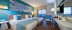 Habitación de hotel con dos camas, un escritorio, una silla, un ventanal con vistas y un adorno en la pared.