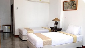 Habitación de hotel con dos camas, una mesita de noche con lámpara, una pequeña mesa y un cuadro en la pared.