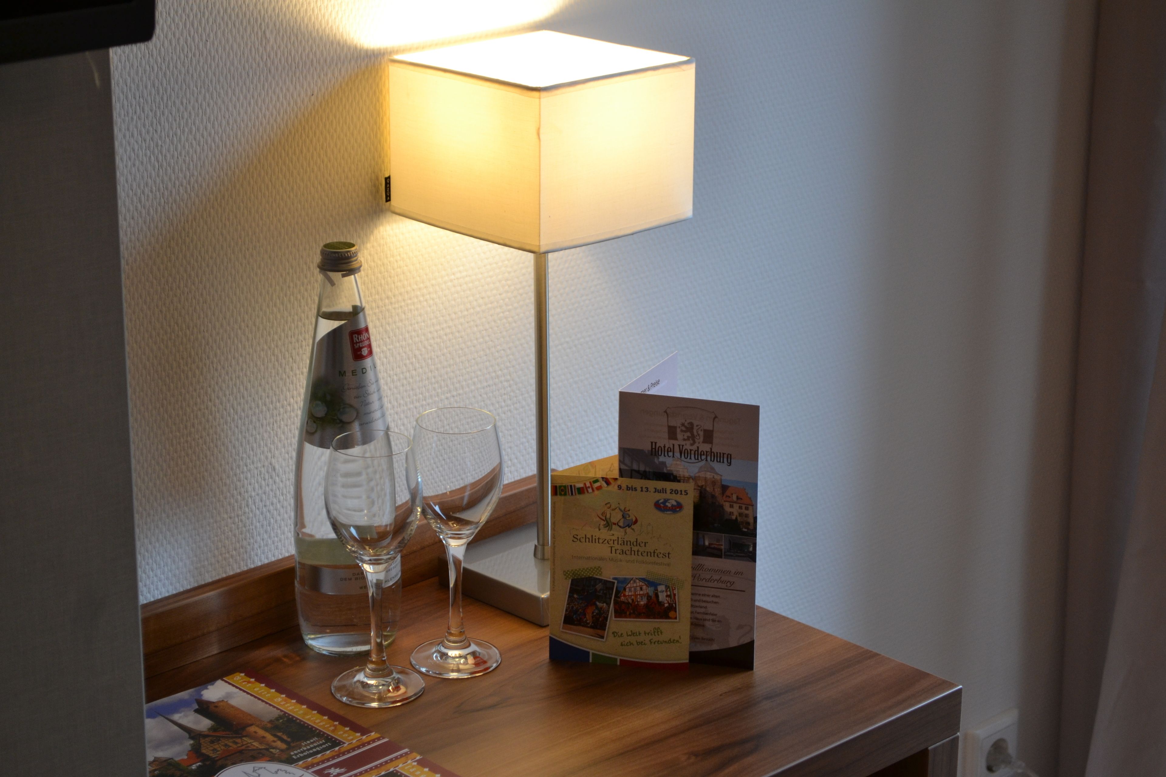 A table with a bottle of wine, two glasses, a brochure, and a lamp.