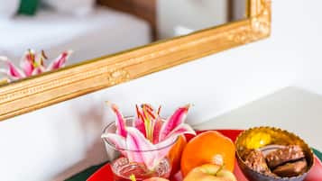 A dining table with a red plate containing fruits and a chocolate dessert, a mirror reflecting a bed with a pink headboard, and a green placemat.
