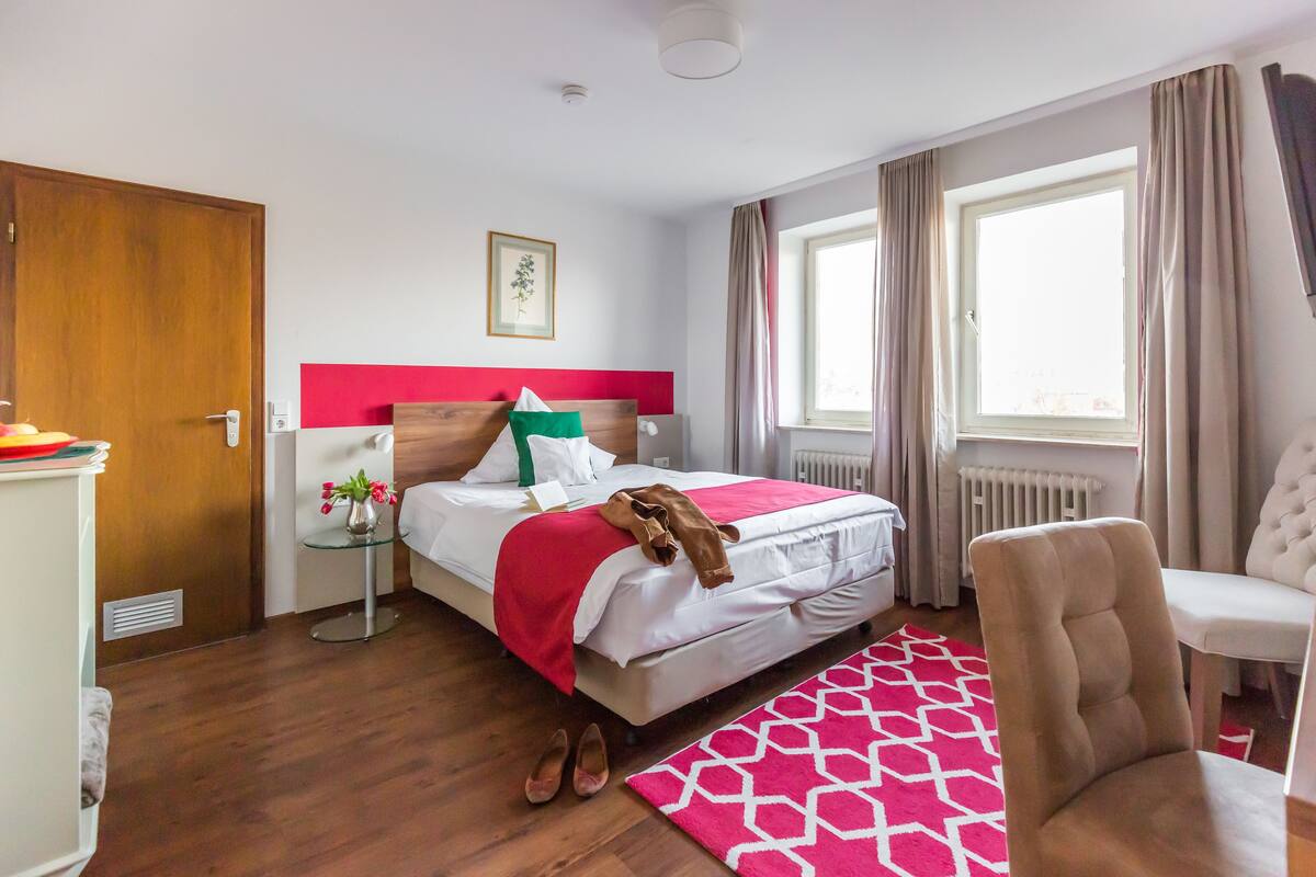 A hotel room with a bed, a chair, a small table, and a window.