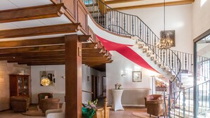 A spacious living area with a wooden staircase, a dog sitting on a rug, and a view of the outside through a glass door. - Hotel Vorderburg (Schlitz)
