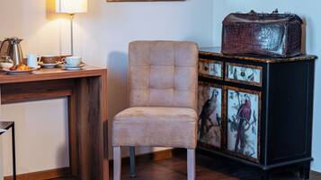 Una habitación con un escritorio de madera, una silla, una lámpara, un armario con obras de arte y una cama.