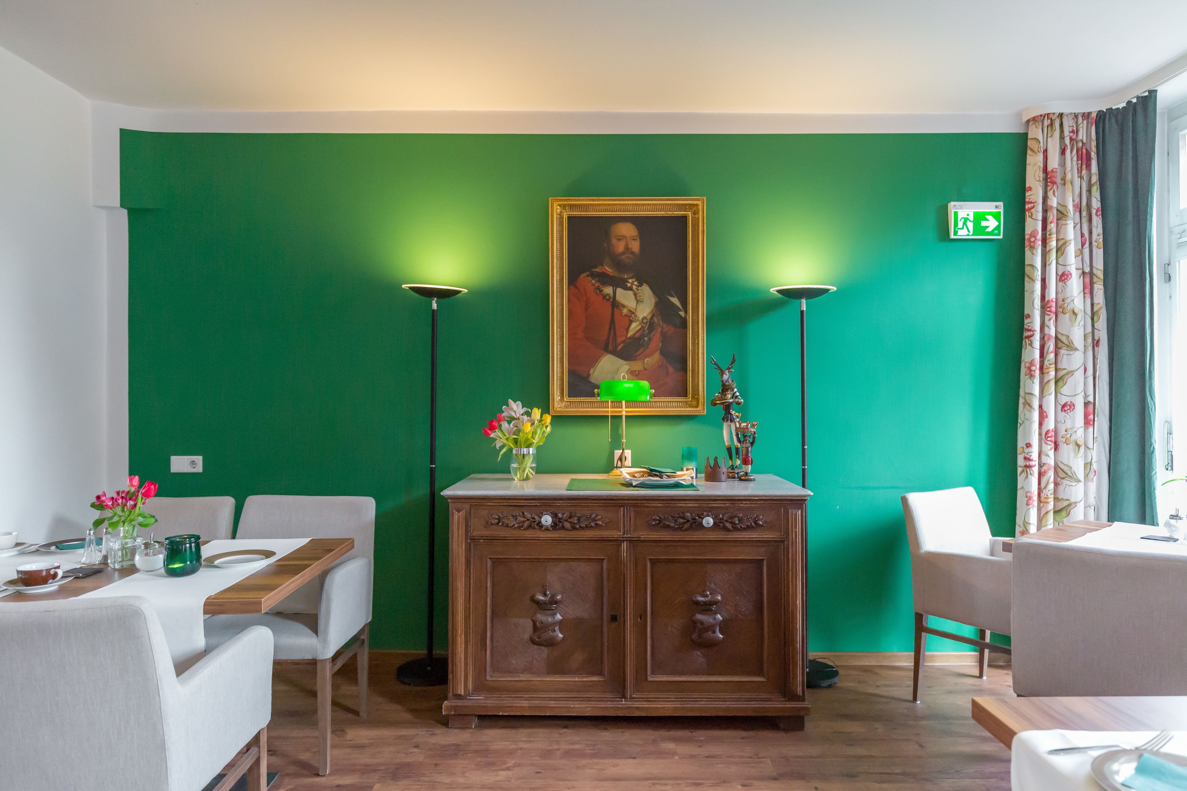 Un comedor con pared verde, un mueble de madera y una mesa lista para dos personas.