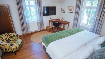 Habitación de hotel con cama, escritorio, silla, televisión y ventana con cortinas.
