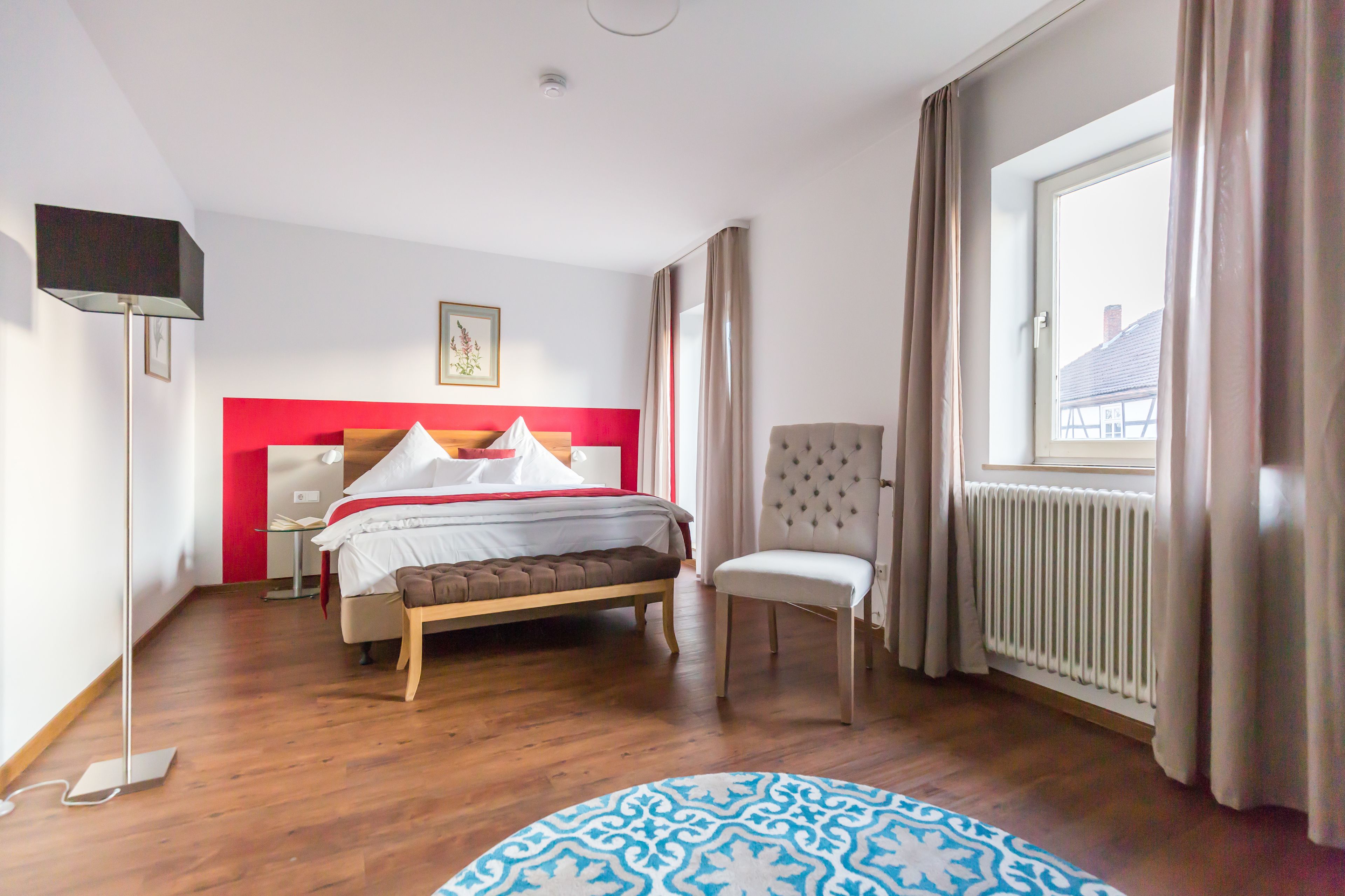 A bedroom with a bed, bedside table, chair, and a window with curtains.