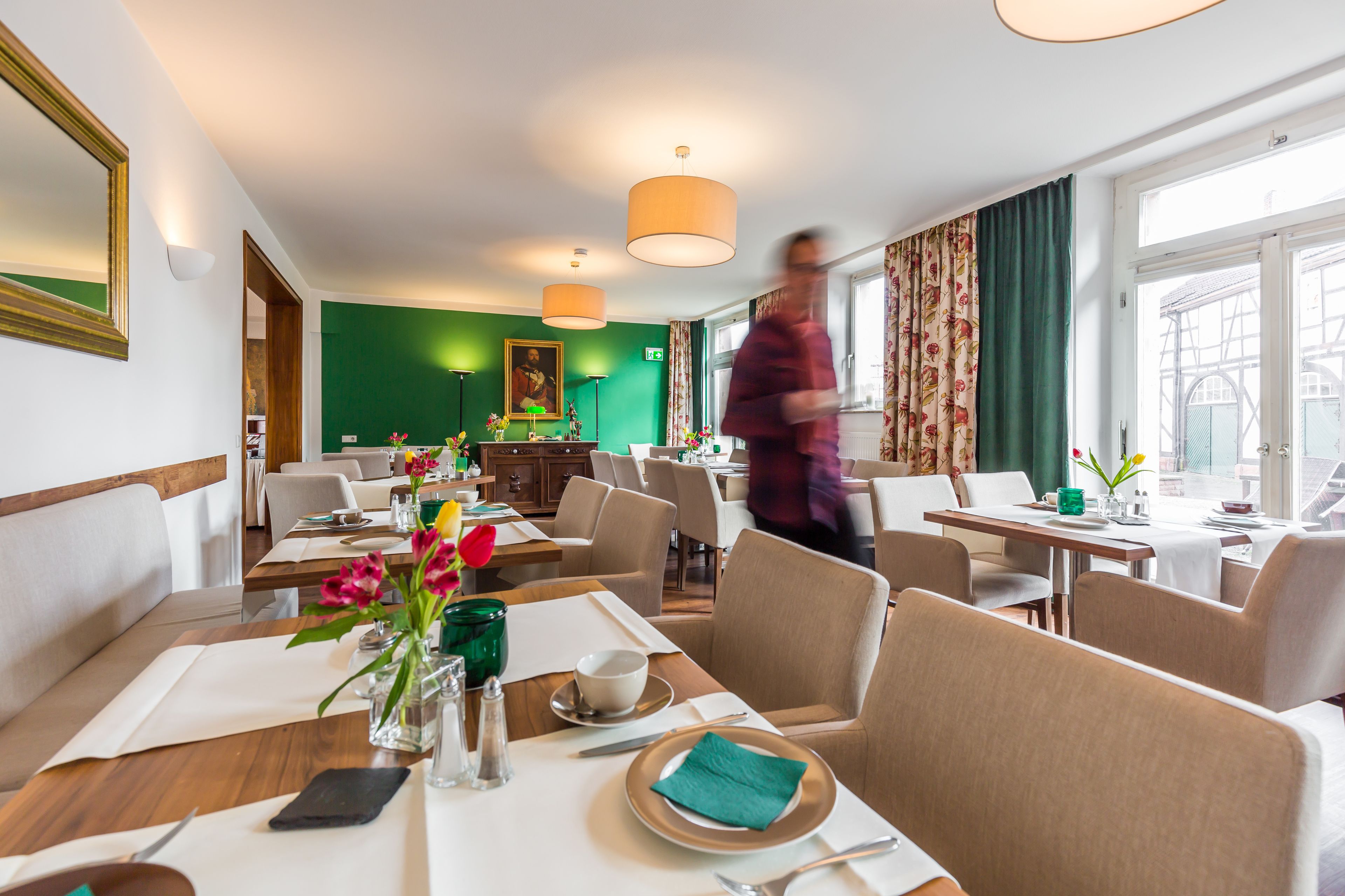Un comedor de hotel con mesas dispuestas para comer, una pared verde y un ventanal con cortinas.