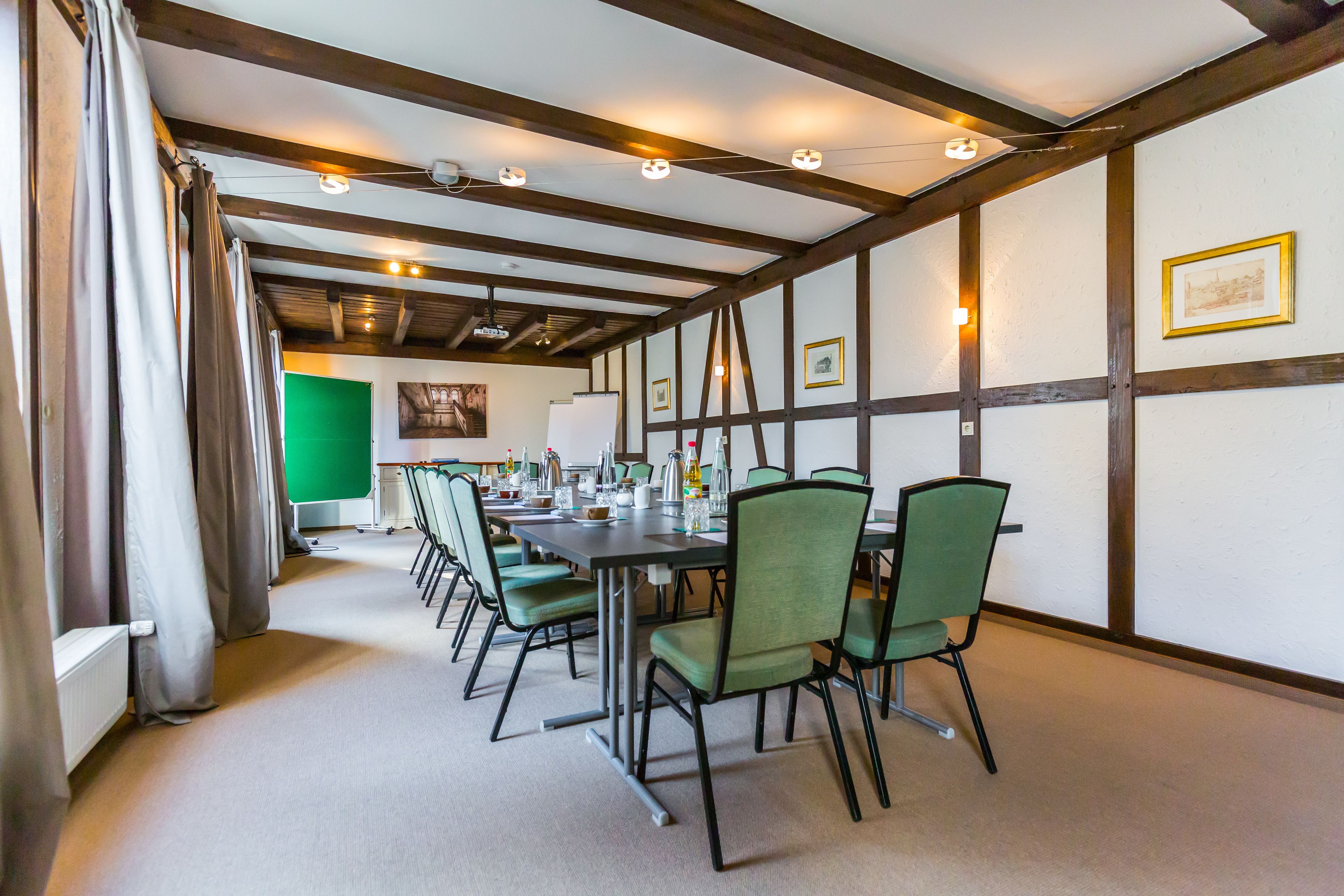 Een vergaderzaal met een lange tafel, groene stoelen en ingelijste foto’s aan de muren.