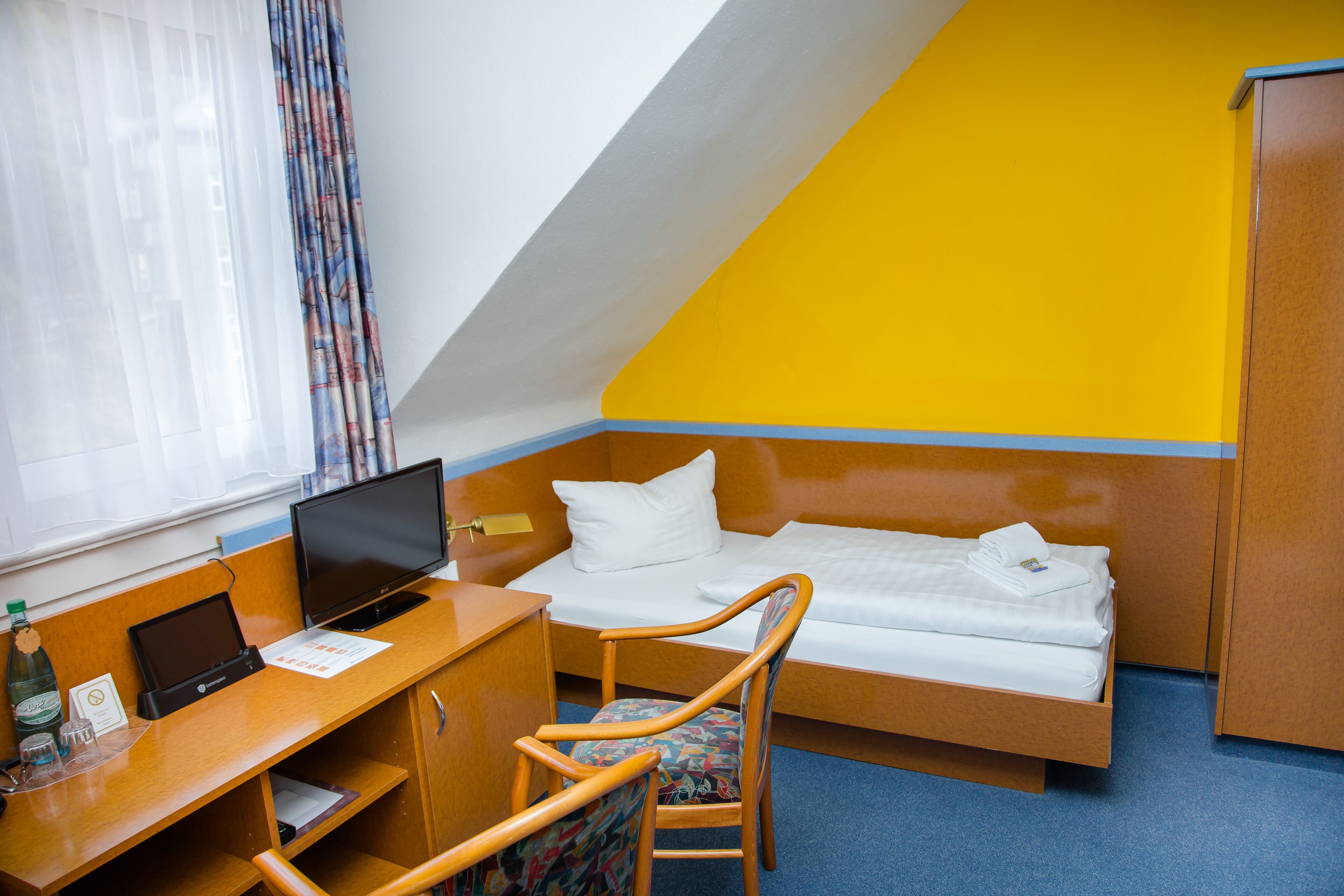 A hotel room with a bed, desk, chair, and a television.