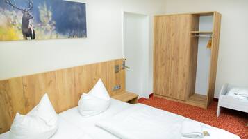 A hotel room with a wooden headboard, a bed with white linens, a wooden wardrobe, and a painting of a deer on the wall.