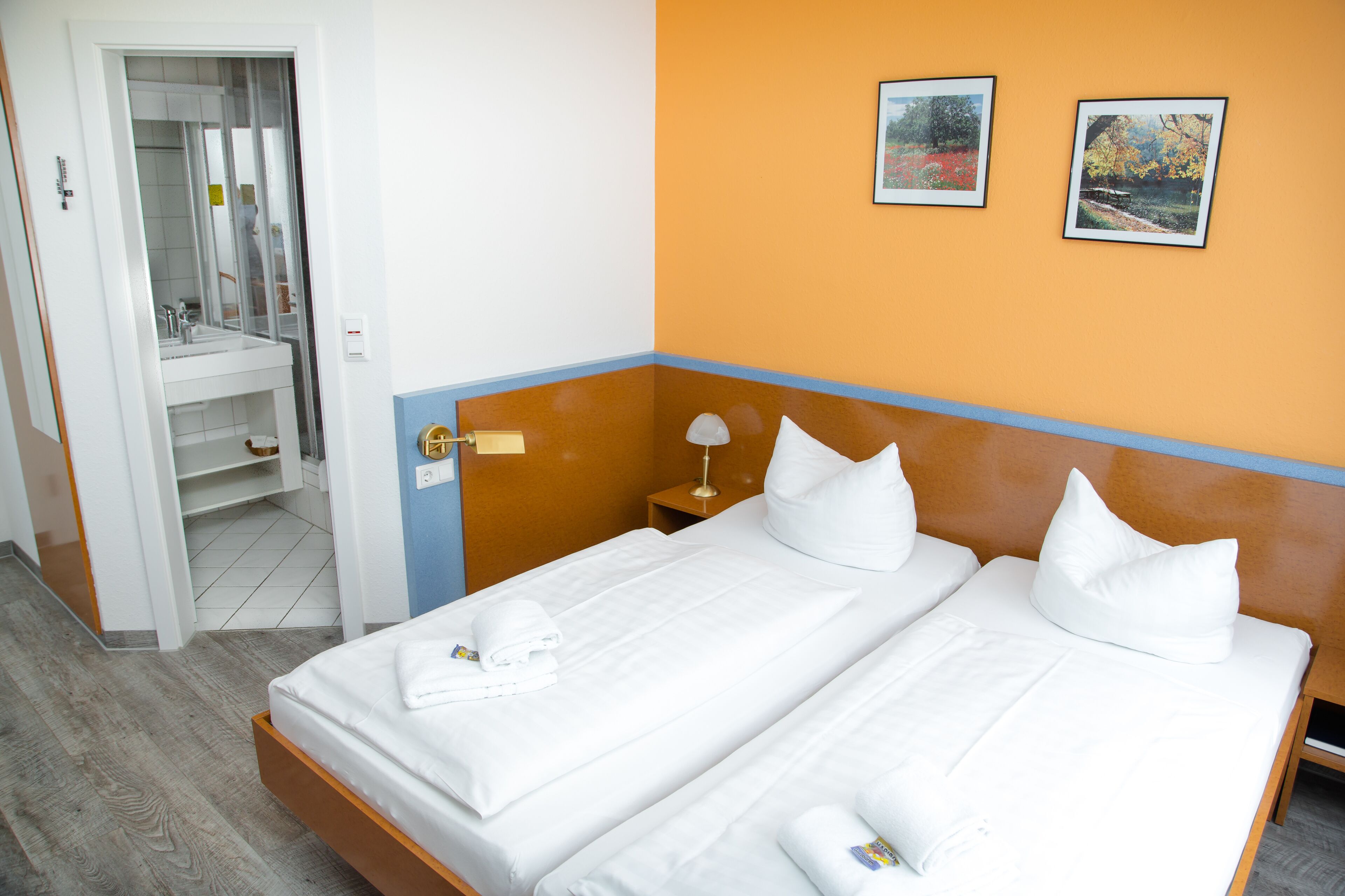 Ein Hotelzimmer mit Doppelbett, Nachttisch, Spiegel und zwei gerahmten Bildern an der Wand.