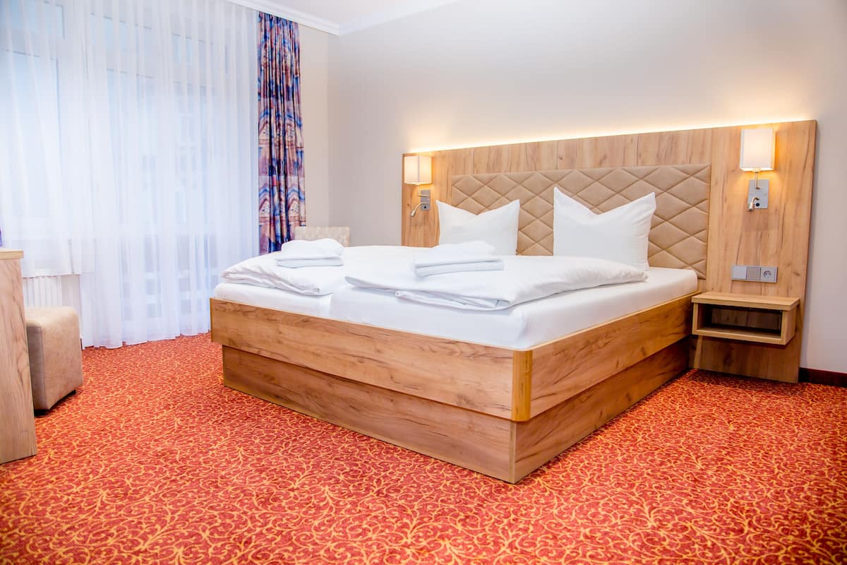 A hotel room with a large bed, wooden headboard, two bedside tables, and a red patterned carpet.