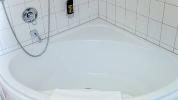 Una bañera grande y vacía con un cabezal de ducha manual y una botella de champú.