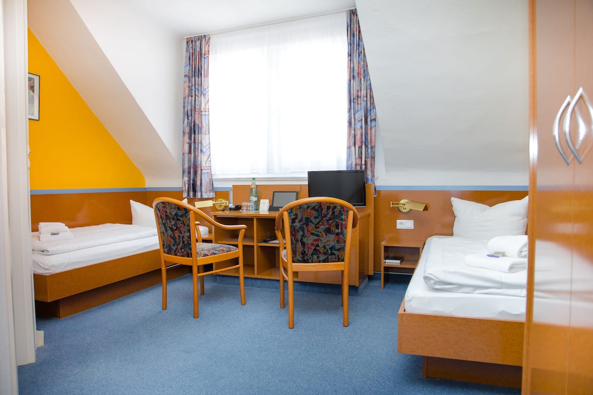 A hotel room with a bed, a desk with a computer, two chairs, and a window with curtains.