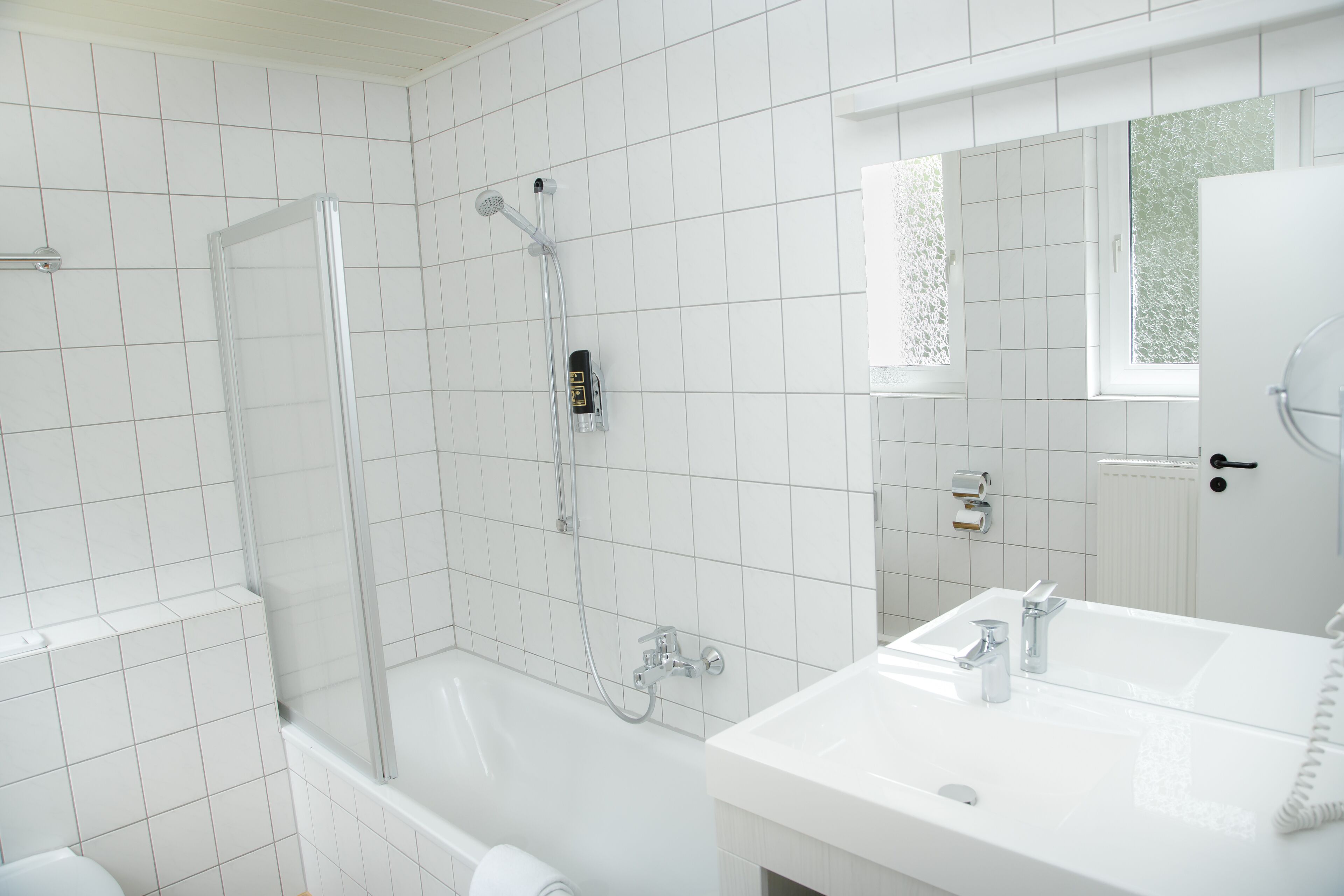 Une salle de bain moderne avec des carreaux blancs, une douche à parois de verre, une baignoire blanche et un meuble-lavabo avec un miroir.