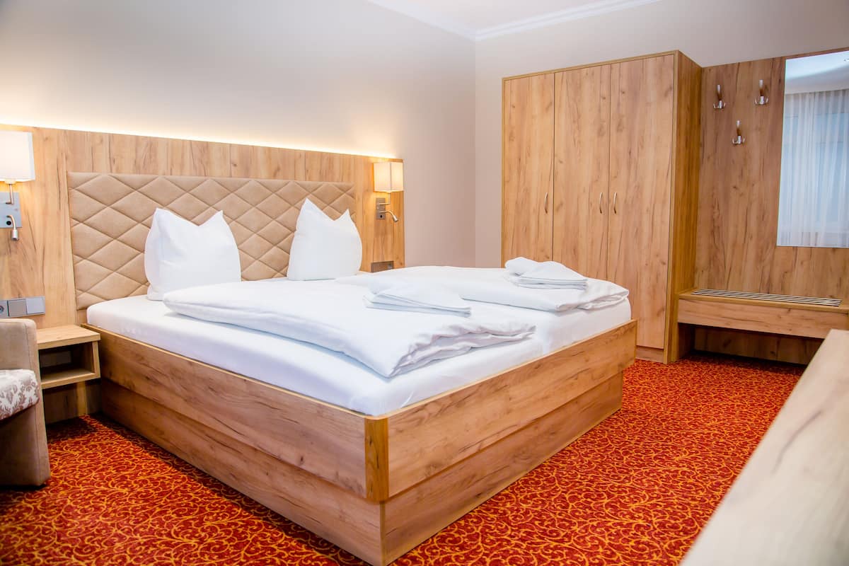 A neatly made bed with a wooden headboard and a red patterned carpet.