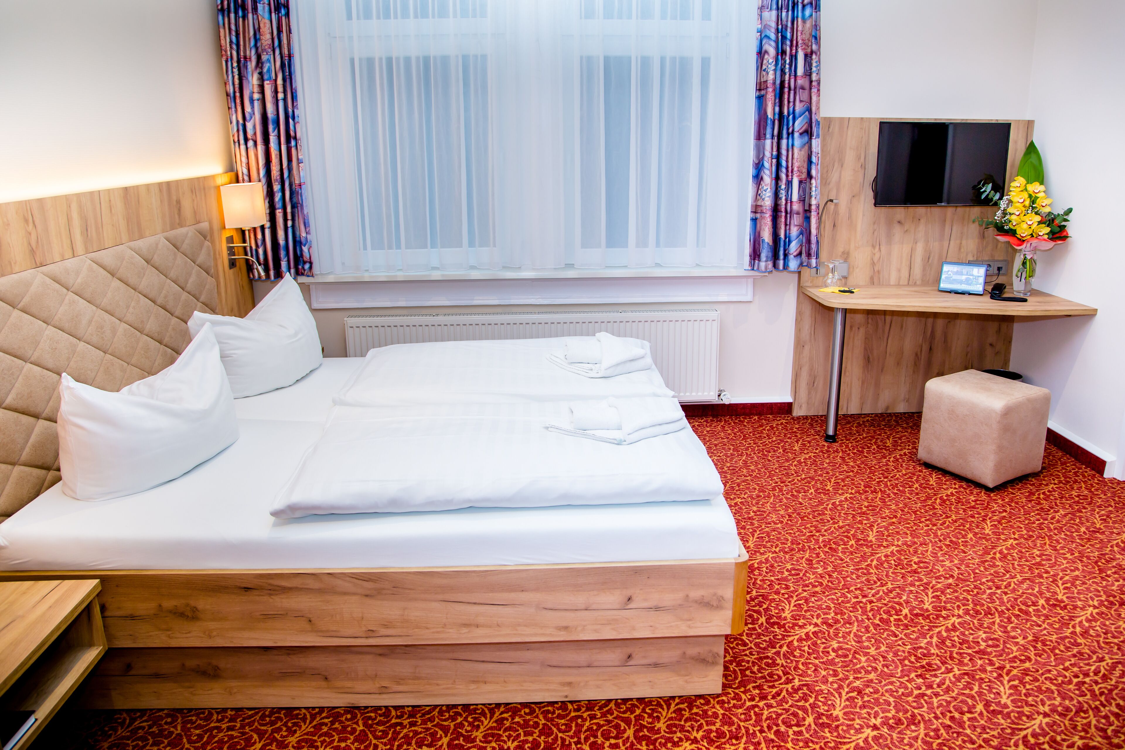 A hotel room with a large bed, a desk, a TV, and a window with curtains.