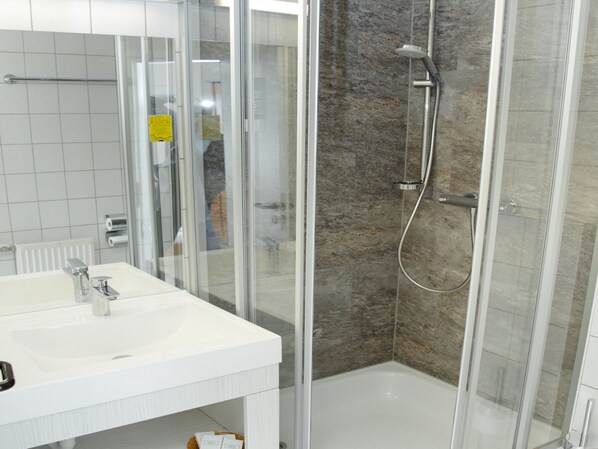 Une salle de bain moderne avec une douche à parois de verre, un lavabo blanc et un mur de douche recouvert de carreaux.