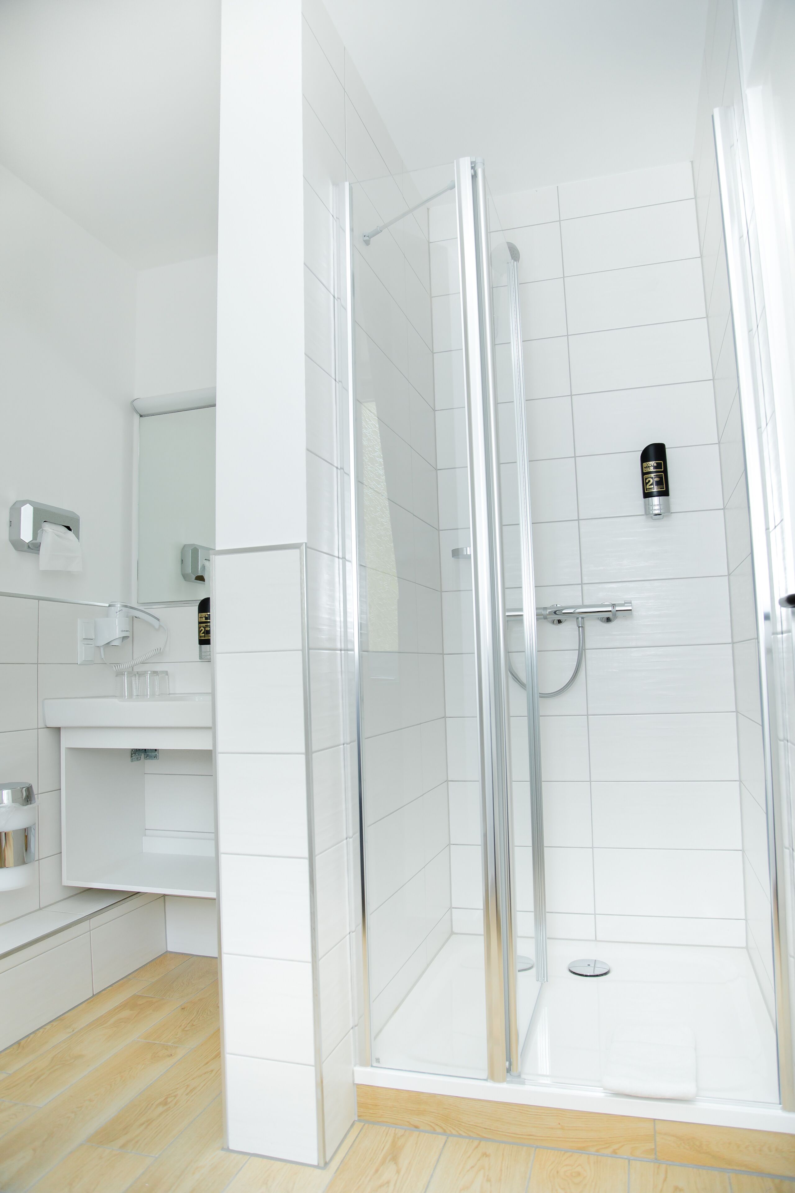 Un baño moderno con cabina de ducha de vidrio, azulejos blancos y suelo de madera.