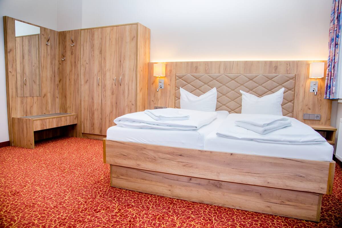 A hotel room with a large bed, wooden wardrobe, and a red patterned carpet.