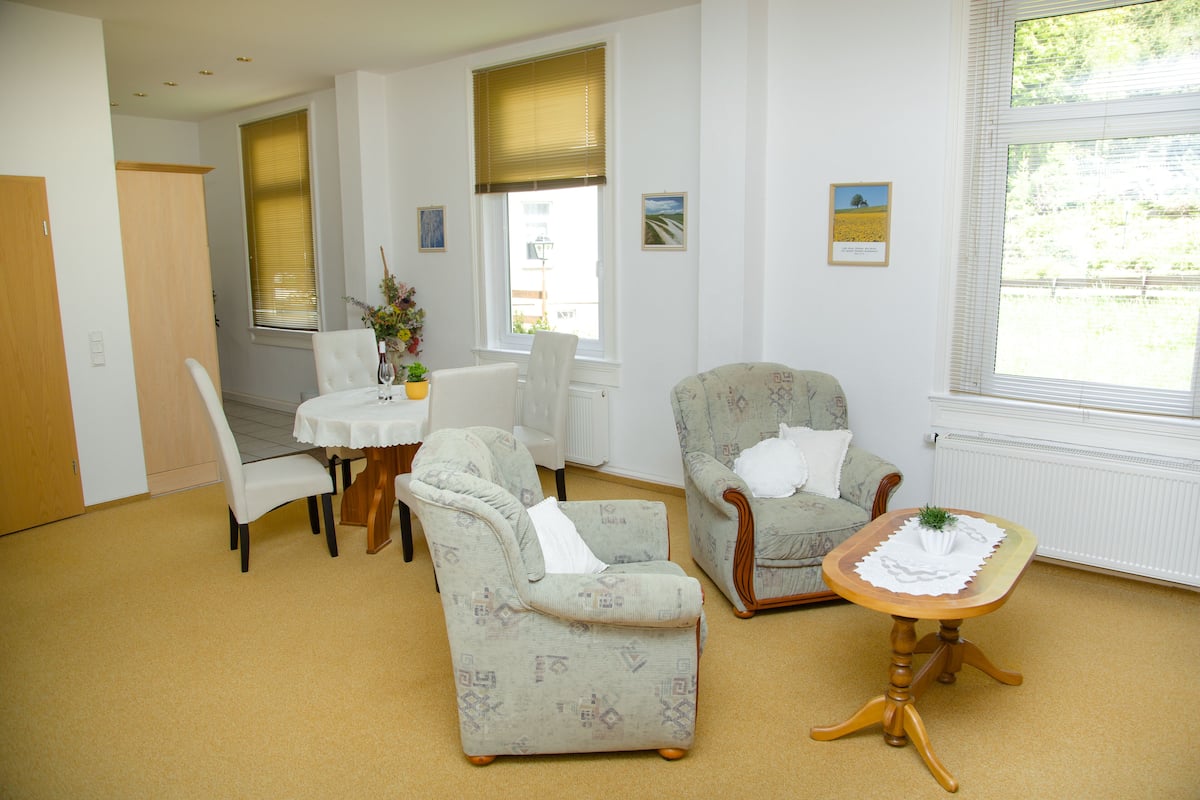 A room with a dining table, two armchairs, a small wooden table, and a radiator.