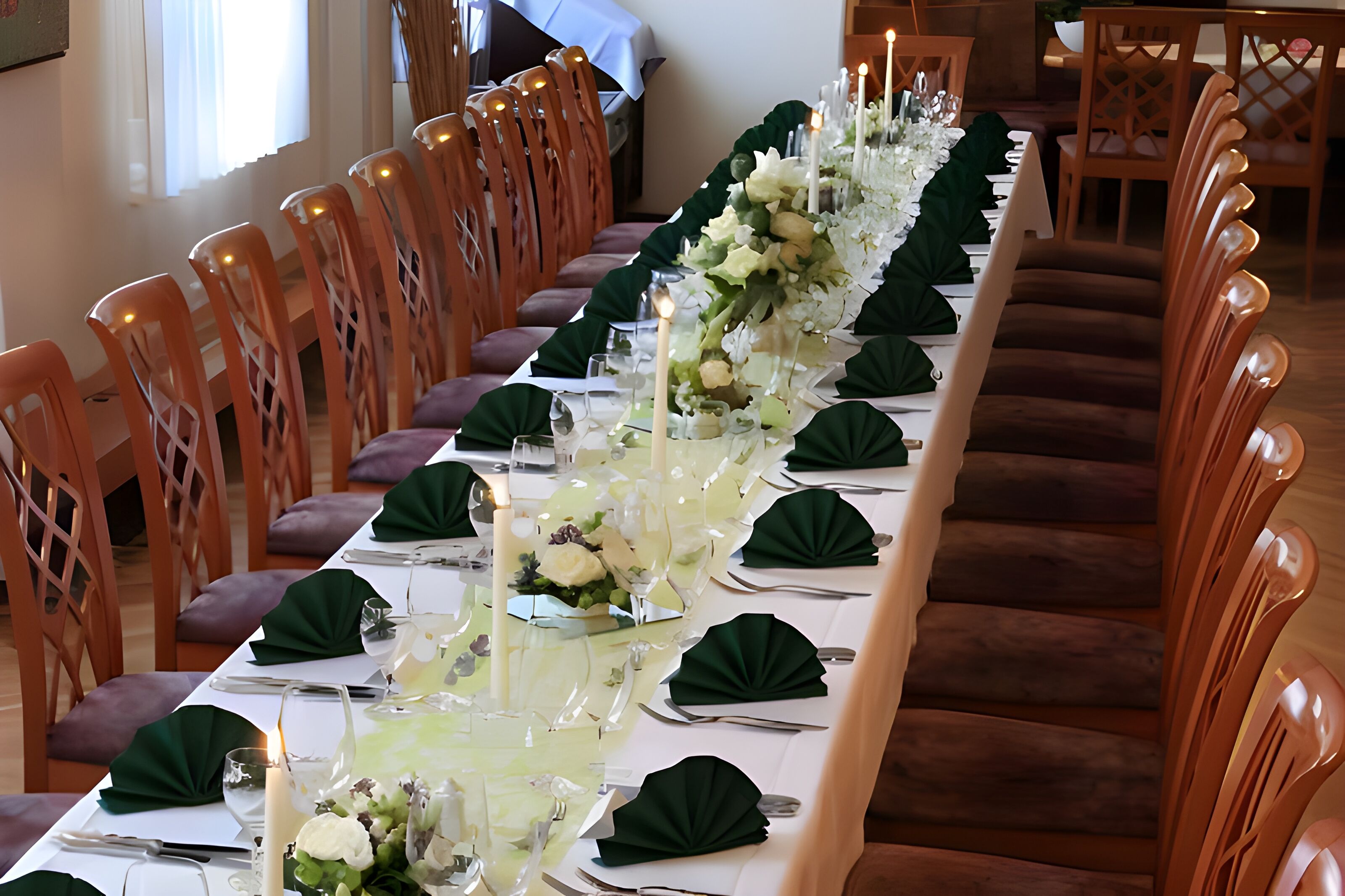 A long dining table set with white tablecloths, green napkins, and floral centerpieces.
