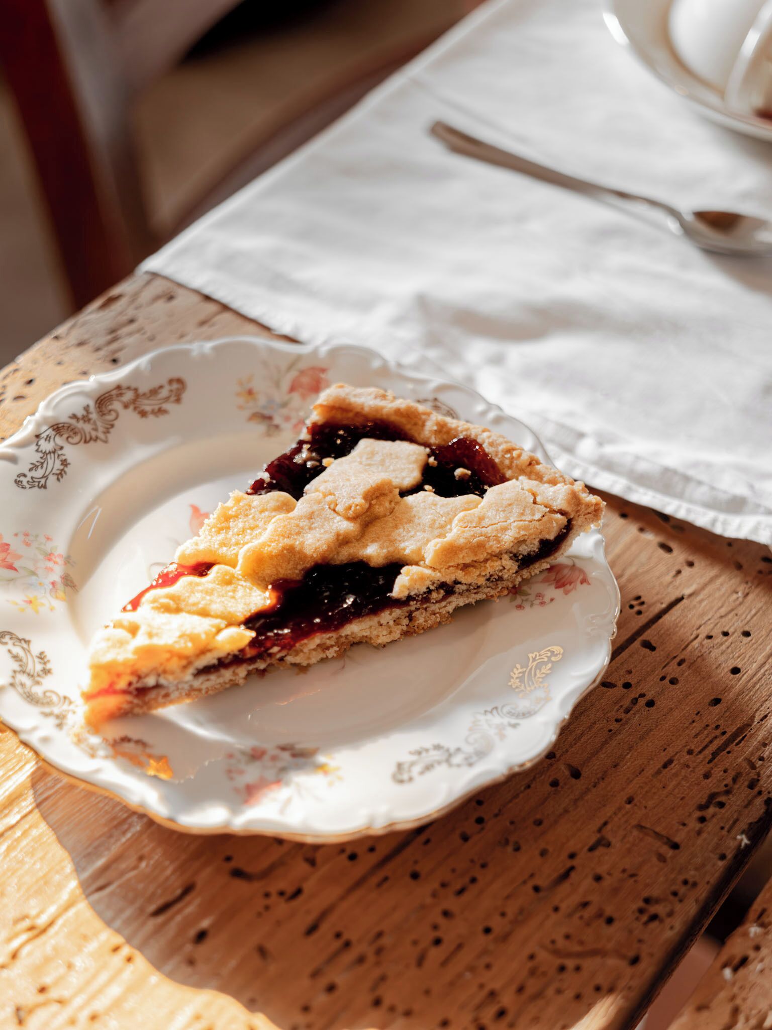 Une part de tarte sur une assiette à motifs floraux, posée sur une table en bois avec une serviette blanche et une cuillère en arrière-plan.