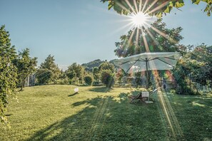 Un patio trasero con césped, un columpio y una silla de jardín bajo un paraguas grande.
