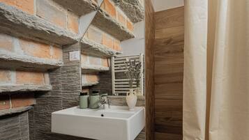 Un bagno con parete in pietra, pavimento in legno, lavandino bianco e tenda per la doccia.