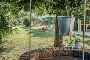 Un jardín con una hamaca, un balde colgante y una planta en maceta.