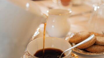 Una taza de café siendo servida en un platito, un plato con galletas y una jarrón al fondo.