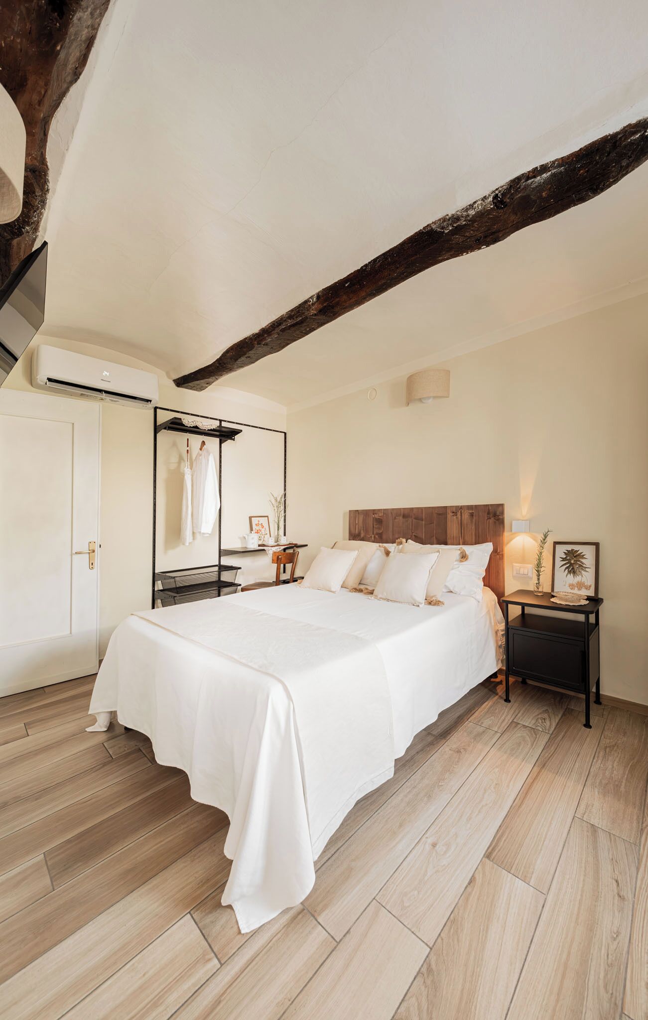 A bedroom with a large bed, wooden beams, a wardrobe, and a mirror.