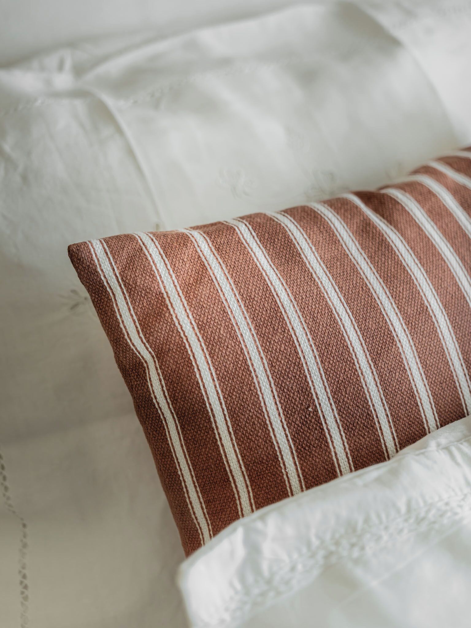 A close-up of a bed with white bedding and a striped pillow.