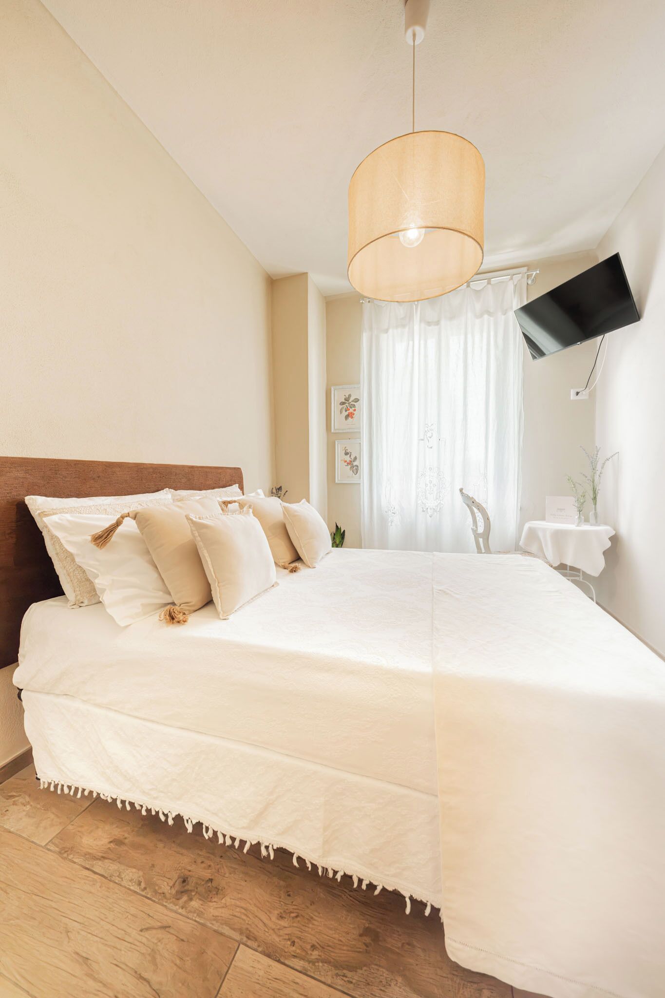 Un dormitorio con cama, televisión montada en la pared y ventana con cortinas.
