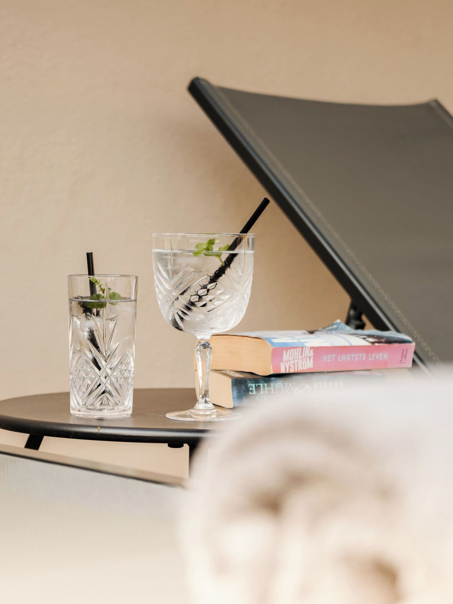 Two glasses of water with straws and mint leaves on a table with a book and a closed laptop.