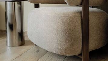 Un sillón moderno con tela texturizada y patas de madera, sobre un piso de madera.