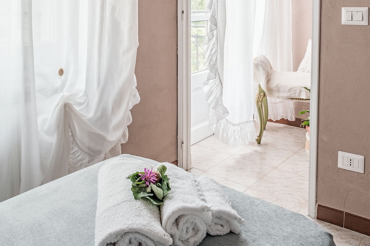 Ein Zimmer mit einem Bett, weißen Vorhängen, einem Spiegel und Blick auf ein weiteres Zimmer.