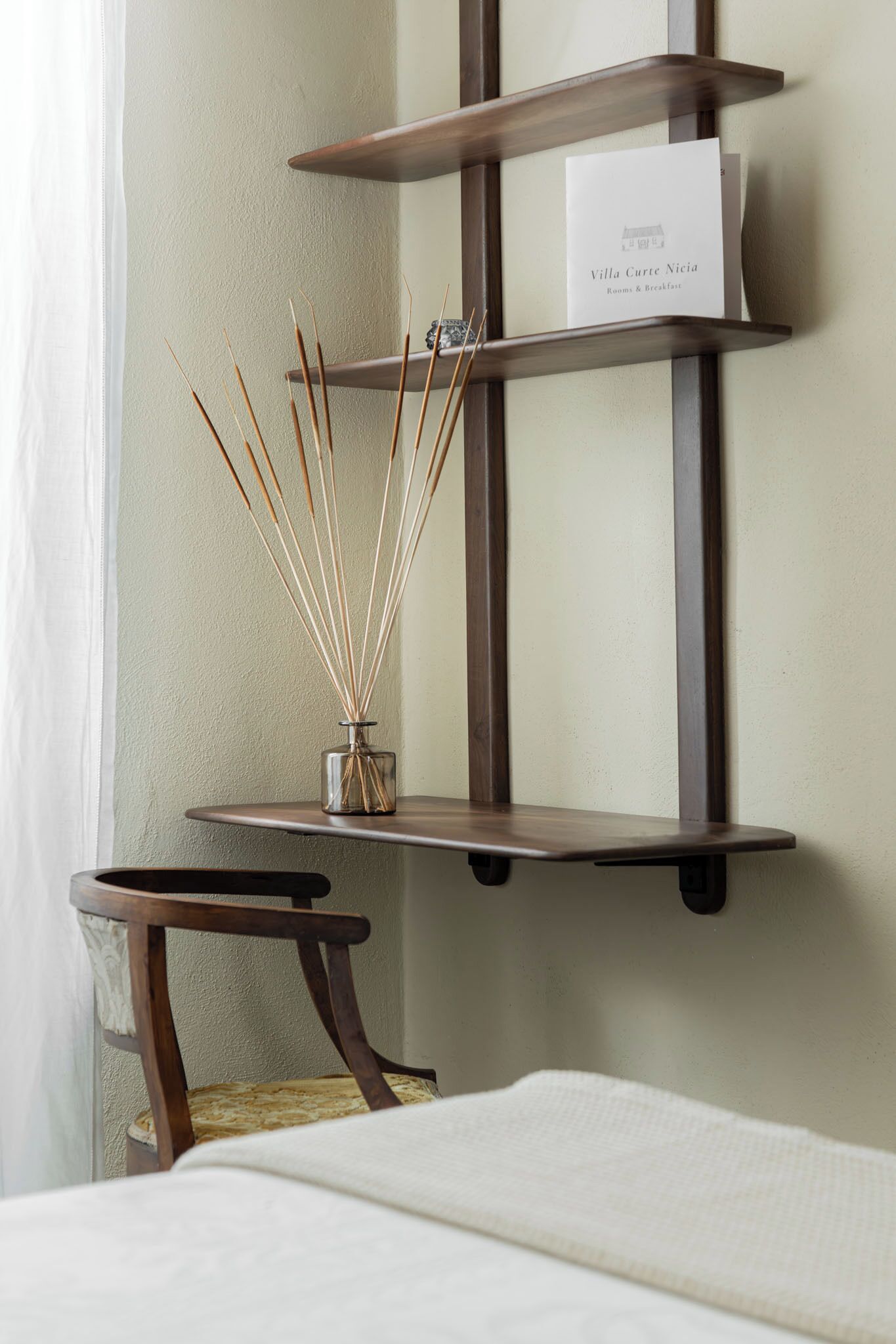 Una scaffalatura angolare con un cartello che indica 'Villa Curte Nigia Rooms & Breakfast' e un diffusore di fragranze in vimini sullo ripiano inferiore.
