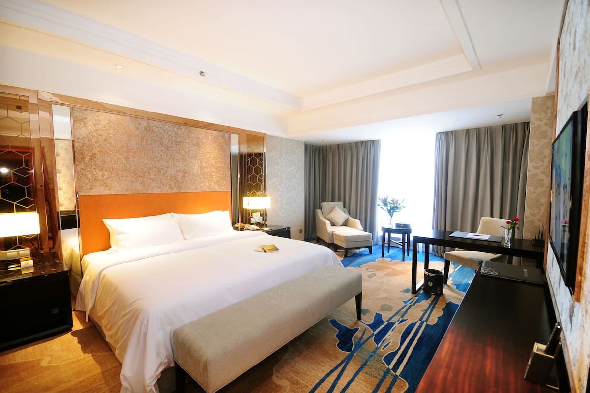 Ein Hotelzimmer mit einem großen Bett, einem Schreibtisch, einem Stuhl und einem Fernseher.