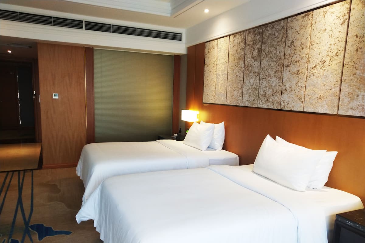 Ein Hotelzimmer mit zwei Betten, einem Holzkopfteil, einem Wandbild und einer Nachttischlampe.
