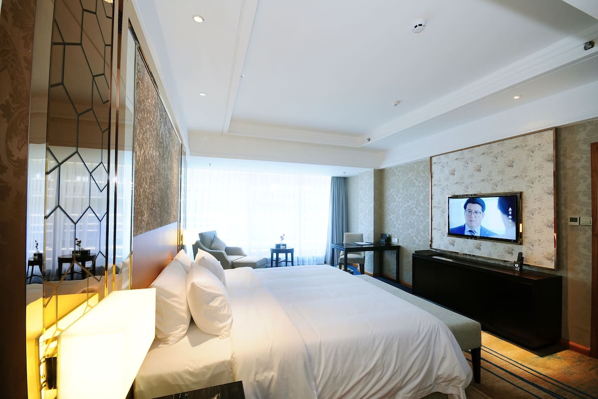 Ein Hotelzimmer mit einem großen Bett, einem Fernseher, einem Schreibtisch und einer Sitzecke.