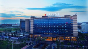 A modern hotel with a glass facade, multiple floors, and a prominent sign on top. - Chengdu Airport Jianguo Hotel (Chengdu)