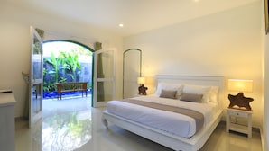 Um quarto espaçoso com uma cama grande, uma mesa de cabeceira com abajur e vista para um jardim através de uma porta aberta.