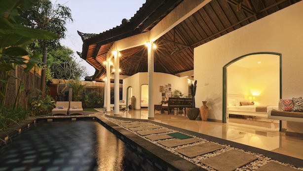 Área da piscina com espreguiçadeiras, espaço de refeições e um alpendre coberto com luzes de fada.