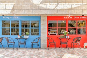 Dos fachadas de café con toldos azules y rojos, sillas de mimbre y suelo de baldosas.