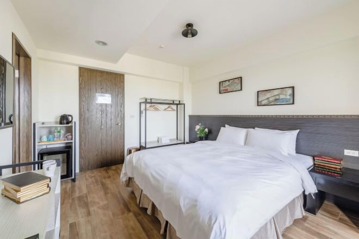A bedroom with a large bed, a desk with a chair, a wardrobe, and a mirror.