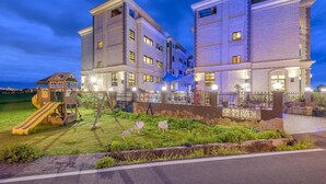 Un edificio de varios pisos con un parque infantil y una zona verde con estatuas de ovejas.