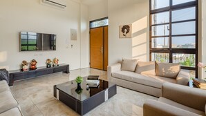 Amplia sala de estar con una gran televisión de pantalla plana, un sofá, una mesa de centro y un amplio ventanal con vistas a la ciudad.