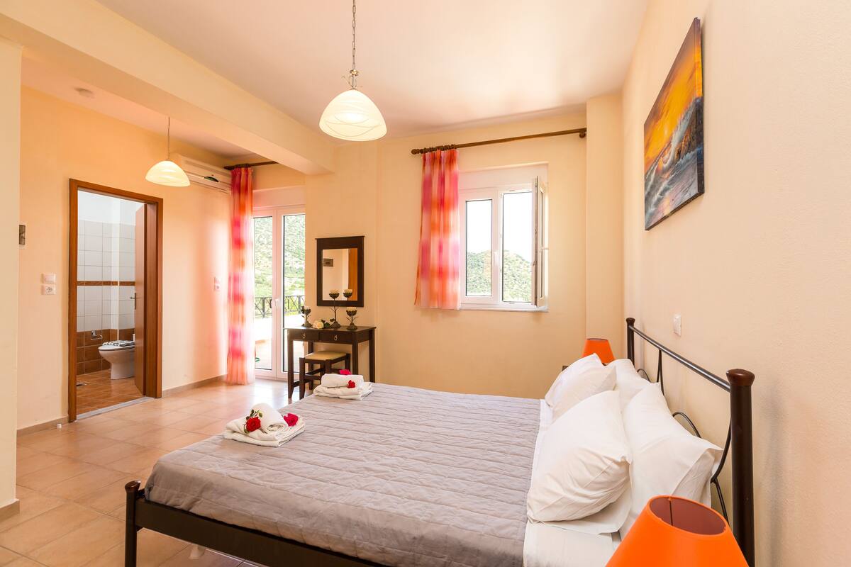 Quarto de hotel com cama, escrivaninha, cadeira, janela com cortinas e um quadro na parede.