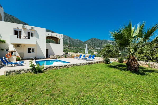 A modern villa with a swimming pool, outdoor seating, and a view of mountains.
